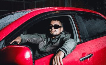 Samochody Volvo dla wysokich kierowców które modele oferują najwięcej miejsca na nogi i nad głową Wysoki mężczyzna w okularach przeciwsłonecznych siedzi w czerwonym Volvo nocą